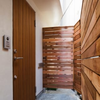 1階　自宅玄関　外観／建物横のアプローチを入るとまず店舗の出入口があり、その先に自宅の玄関扉がある。周囲はウッドフェンスで囲み、プライベート感を確保
