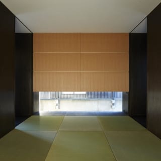 １階　和室／写真正面のタモ材を使用した大きな造り付け収納の明るい色合いを、壁面のダークブラウンが引き締め洗練された印象。縁のない琉球畳を選び、よりオリエンタルな雰囲気になっている。 窓越しには公園のフェンスで圧迫感があるため、窓は低く配置した