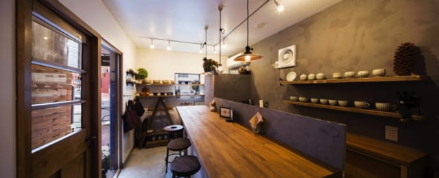 1階　店舗／奥さまが作家から買い付けたうつわが並ぶ店内。側面のガラス窓と、大通り側に設けた窓で採光と開放感を得ている。おいしい料理とホッとくつろげる雰囲気が人気で、昼どきは近隣の会社員でにぎわう
