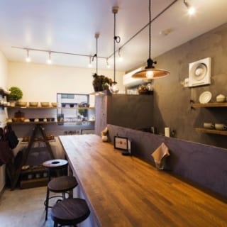 1階　店舗／奥さまが作家から買い付けたうつわが並ぶ店内。側面のガラス窓と、大通り側に設けた窓で採光と開放感を得ている。おいしい料理とホッとくつろげる雰囲気が人気で、昼どきは近隣の会社員でにぎわう