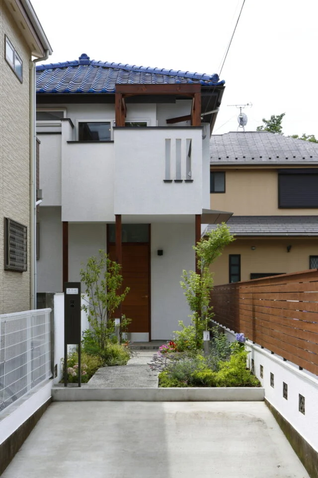外観　玄関／青い屋根はそのままに、新たにバルコニーを設置。ウッドフェンスでナチュラル感を演出。アプローチのゆるやかなカーブが、植栽の小道を通る楽しさをもたらす