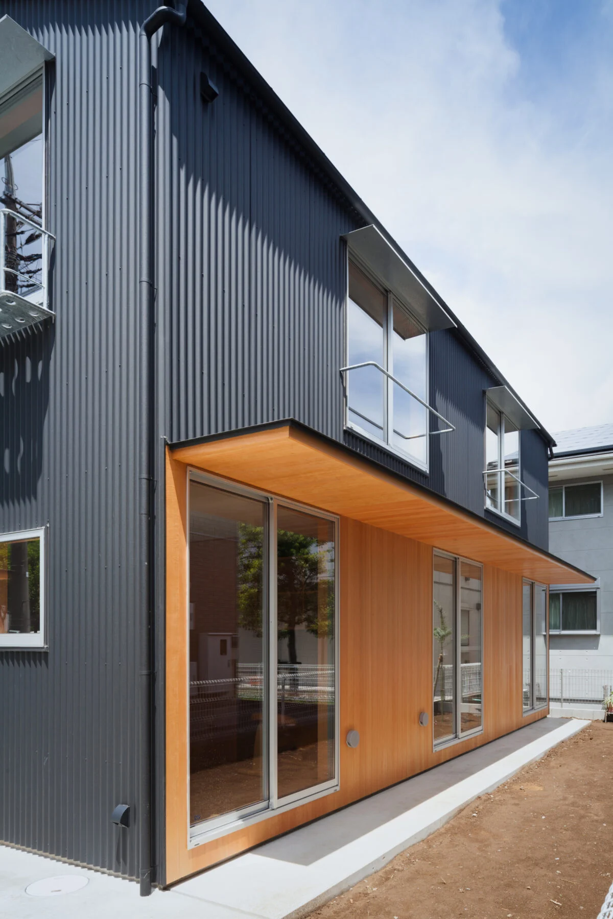 軒下。１階建物東側は、個室が三室並び、個室の外側には外壁と軒裏にピーラー材が貼られた軒下空間が。２階の二つの窓には布団干し用のバーが設けられている