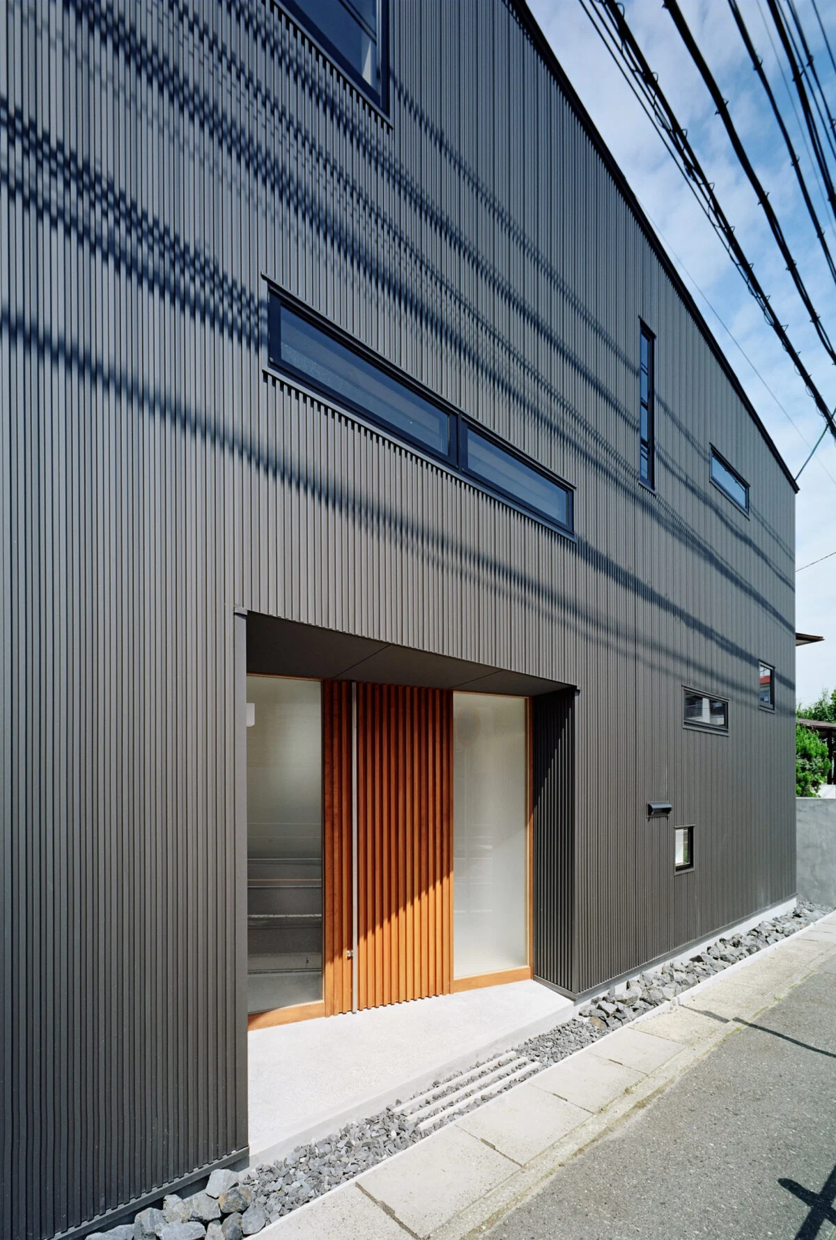 建築事務所の入口は東側。外壁材にガルバニウム鋼板を用いることで、木製ルーバーで覆われた住宅部とは異なる印象に