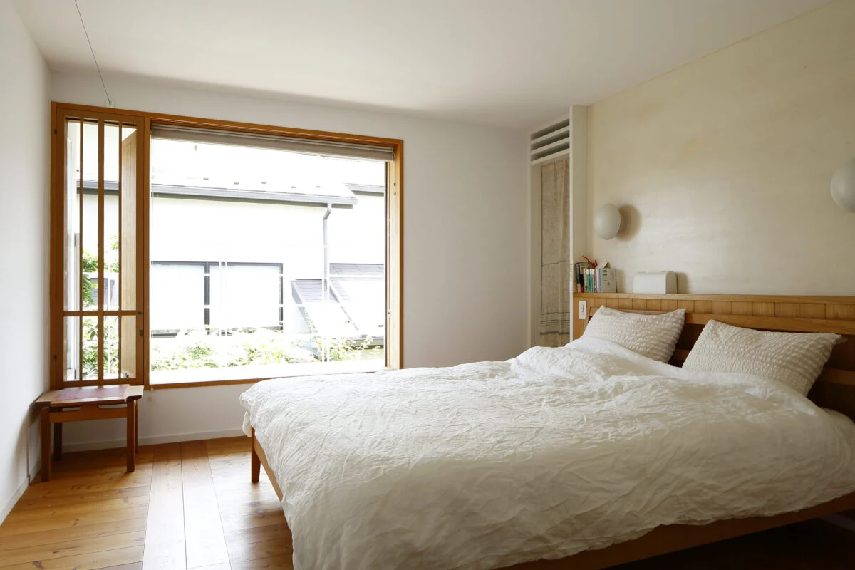 2階主寝室。木製の窓枠が、シンプルな白い部屋によく映える。窓を開け放しておくこともできるよう、左側に細い通気用の窓も設けている。窓の外は洗濯物などを干せるバルコニー