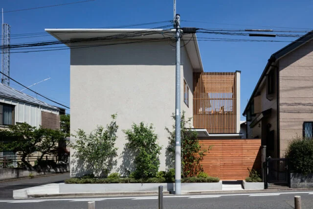 敷地は、東西北が道路に面する角地。建物の背面にあたる南側は隣家が迫り採光を望みにくい。そこで、敷地の南側に広いデッキを設け、デッキに入る光が家中に行きわたるプランで採光を確保。その分、道路面は壁が多くなったが、植栽によっていきいきとした表情を加えている