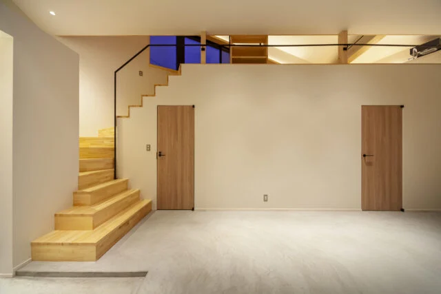 1階玄関ホールの階段まわり。左の扉がトイレで、右の扉が寝室。さらに右に行くと洗面＆浴室がある。上部のアキから2階ダイニングが少し見えて視線が抜け、一体感と開放感が生まれている