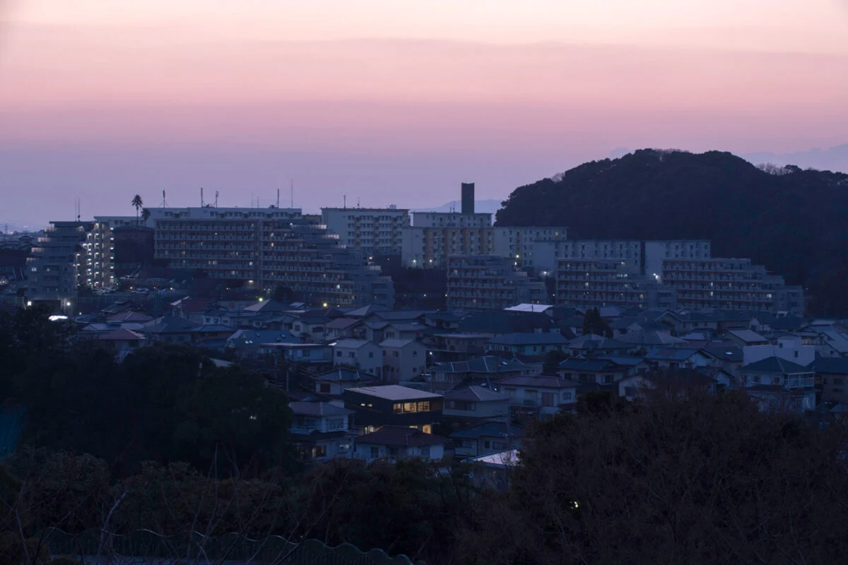 J邸が立つ住宅街を北から見た夕景。明かりがともる時間帯になると、北に大きな窓がない家が多い中、北向きに大開口を設けたJ邸がひときわ目立つ
