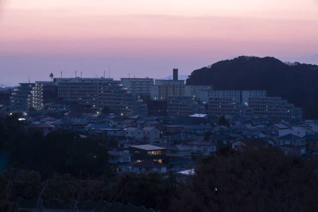 J邸が立つ住宅街を北から見た夕景。明かりがともる時間帯になると、北に大きな窓がない家が多い中、北向きに大開口を設けたJ邸がひときわ目立つ