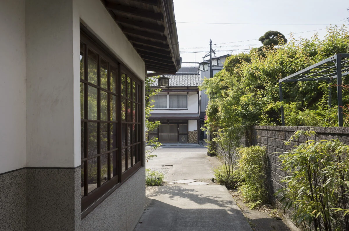 道路から玄関へのアプローチ。写真奥が道路で、右側に息子さん夫妻の住まいがある。左の窓は施主さまの寝室の窓。改修前の古い木枠を再利用して風情を残しつつ、内窓をつけて断熱性能を高めた