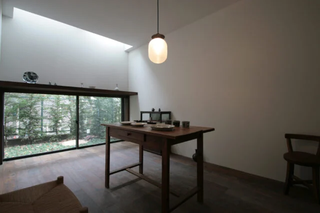1階応接間。H邸は旗竿地のため、建物の2カ所をL字に凹ませ、2つの小さな庭をつくって「庭に面した窓」を各所に設置。応接間は隣家の窓と相対しない低い位置に大窓があり、裏庭の緑が見える。窓の上は作品を飾る造作棚。天窓の光がスポットライトのように作品を照らし出す