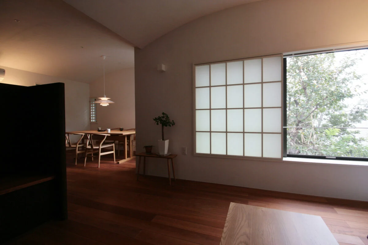 2階のリビングには、屋外の景色を大きく切り取り、緑に寄り添うような窓をつくった。あえて低めの位置にすることで、2階でも屋外とつながる感覚を強めている。隣家の視線を気にせずにすむよう、半分は障子で隠して光だけを入れている