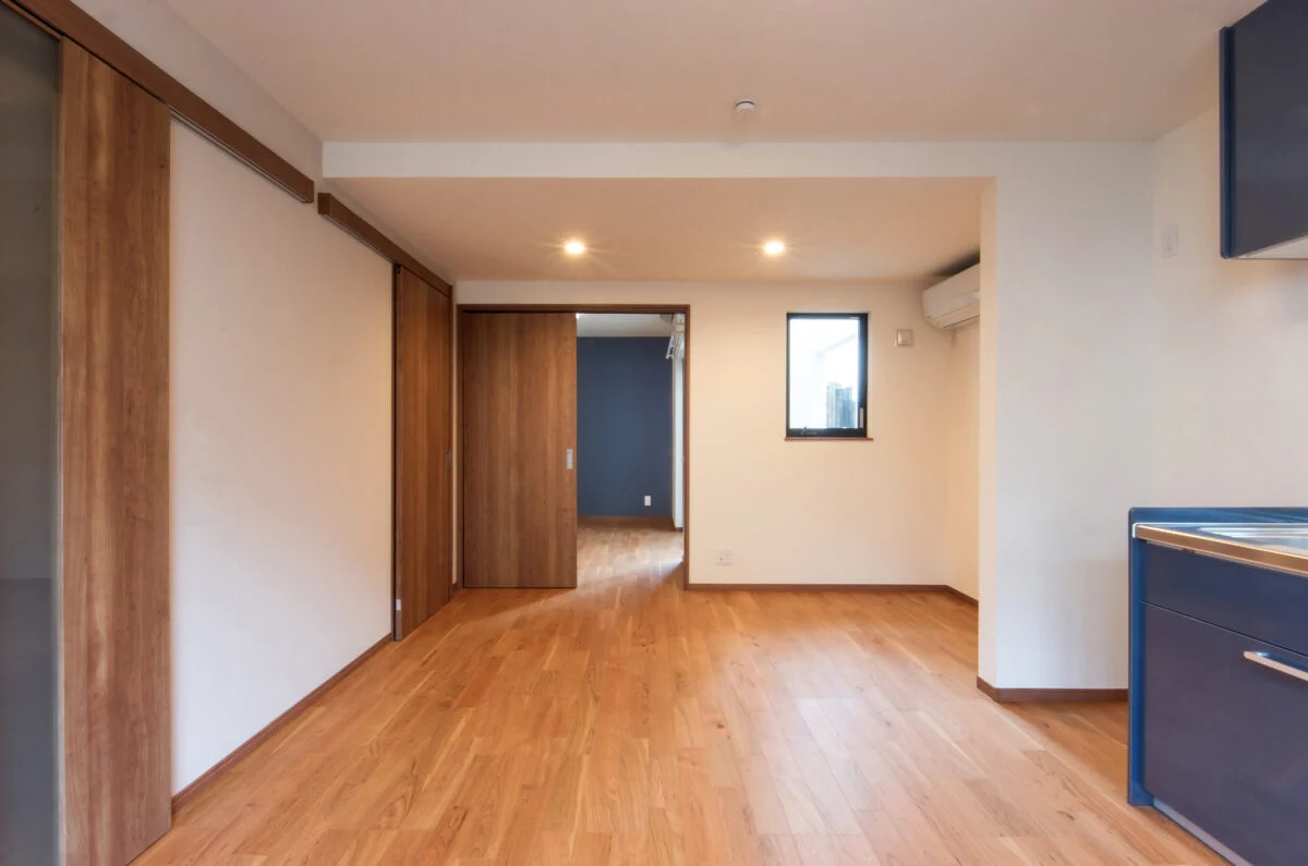 1階賃貸A住戸、LDKから寝室までを見る。一続きになった空間は道路側にリビング、奥に寝室を配置し、騒音も考慮した。道路側にある窓に加えて、写真正面の窓からもテラスを通して光が入るためLDKはいつでも明るい。寝室からはテラスに出ることもできる