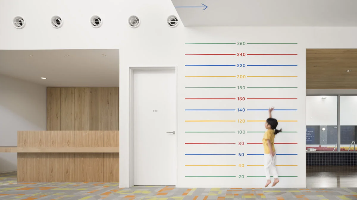 【1階/子どもゾーン】レセプション脇の壁には高さを示すラインを入れた。ジャンプ力を簡単にチェックできるため、喜んでチャレンジする子どもが続出