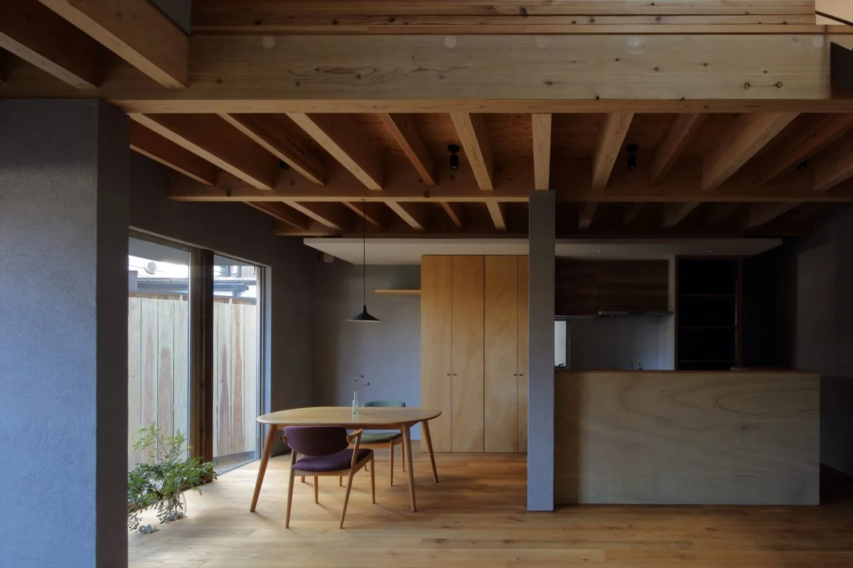 1階リビングからダイニング、キッチンを見る。壁は建物を支える力強さを表現し家に必要な安心感が生まれた。キッチンに立つと遮るものなく1階の空間が見渡せるほか、吹き抜けを通して2階の気配が届き家全体の様子を把握できる。正面中央、木製の造作収納はパントリーとして使用