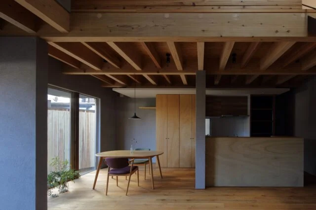 1階リビングからダイニング、キッチンを見る。壁は建物を支える力強さを表現し家に必要な安心感が生まれた。キッチンに立つと遮るものなく1階の空間が見渡せるほか、吹き抜けを通して2階の気配が届き家全体の様子を把握できる。正面中央、木製の造作収納はパントリーとして使用