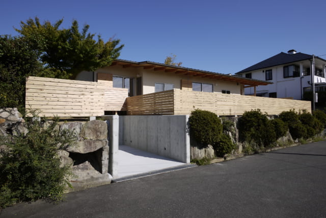 杉材を贅沢に使用した囲いが印象的な外観。その下の石垣は以前の家を建てた当時と法律が変わり、撤去の可能性もあったが「こんないい雰囲気の石垣を壊すのはもったいない」と稲田さんが市と相談、無事に残すことができた。写真左の大きなモミジもギリギリの掘削で残したという