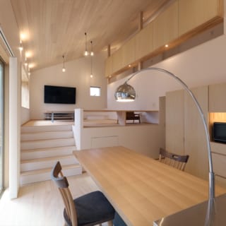 ダイニングは２階から屋根がなだらかに下り、吹き抜けでありつつ1.5階程度の天井高。加えて画像奥のリビングは中２階のような床の高さで、より落ち着く空間となった。リビングは子どもたちが床に座るとキッチンやダイニングから目が合う高さに計画。コミュニケーションを取りやすい