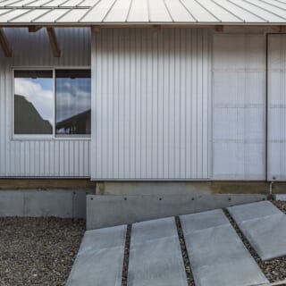 道路側から建物を見る。画像右、玄関には透光性のある真っ白な断熱材とポリカーボネートを組み合わせた引き戸を設けた。大きな建具だが、ガラスほど重くなく開閉しやすい利点もある。屋根の一角には天窓があり、奥行きが深い庇の下をふわりと明るくする