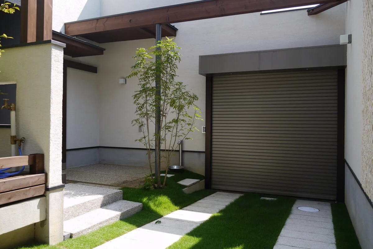 中庭、シャッター裏。外観は濃い色合いだが、左に見える庇の下にある扉を開けると見える景色は白く、明るくなる。「敷地内に入ると木々も見えます。軽やかな気分で室内へと入っていただけるように計画しました」と稲田さん