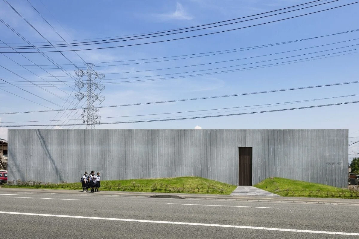 40mの壁が印象的なファサード。甲府市内の幹線道路沿いという都市スケールにマッチする、堂々たる佇まいだ。陰影のある出目地コンクリートと芝のマウンドによるシンプルな構成は、幹線道路の無機質な景色にうるおいをプラス。公園のような存在感がある
