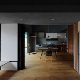 建物西南角の仏間から見たDK。天井が高いDKに比べて、仏間の天井は低く抑えられている。また、DKはグレーの漆喰の塗り壁であるのに対し、仏間の壁は土佐和紙仕上げ。写真左側の窓は、上部がフィックスで下部は開閉できる。障子紙を太鼓張りにした開き戸がカーテン代わりとなる
