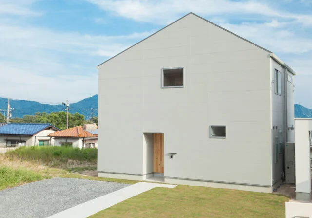 家は1階と２階と外周が同じ、総2階建て。庇がなくシンプルなフォルムで、構造に無駄がないためコストが抑えられた。以前は町の集会所があった一角という「八坂の家」の敷地。アクセスがよいことに加えて、見晴らしなどの立地条件もよかったため、お施主さまは購入を決めた