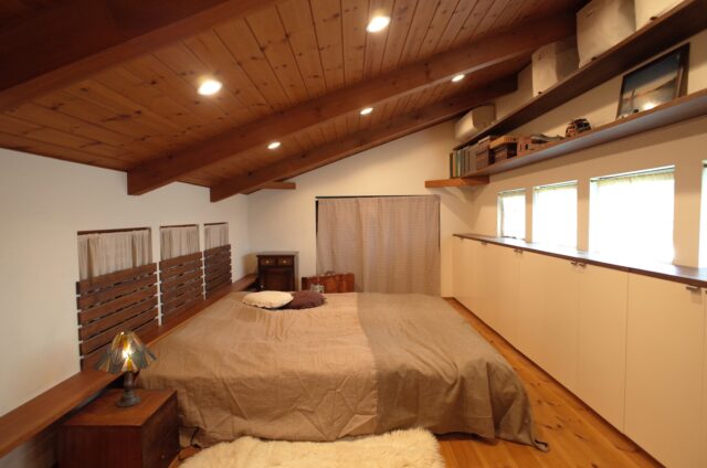 2階主寝室。写真左の3つの小窓のカーテンを開けると、吹抜けを介してリビングを見下ろせる。1階と2階は1つの屋根で覆われており、天井は北（写真右）に向かって高くなる勾配天井。北側はずらりと横窓が設けられ、安定したやさしい光が入ってくる