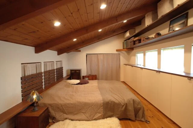 2階主寝室。写真左の3つの小窓のカーテンを開けると、吹抜けを介してリビングを見下ろせる。1階と2階は1つの屋根で覆われており、天井は北（写真右）に向かって高くなる勾配天井。北側はずらりと横窓が設けられ、安定したやさしい光が入ってくる