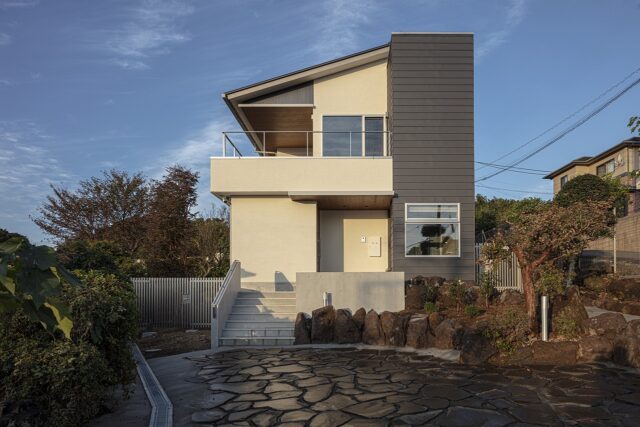 海側から見た外観。家の右側に浴室の窓がある。玄関へは階段を上るほか、画像右に設けられたスロープを使ってもアクセスできる。２階のテラスは眺望の邪魔にならないよう、柱をなくし、また手すりも可能な限りシンプルな設えとした