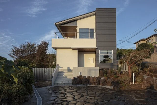 海側から見た外観。家の右側に浴室の窓がある。玄関へは階段を上るほか、画像右に設けられたスロープを使ってもアクセスできる。２階のテラスは眺望の邪魔にならないよう、柱をなくし、また手すりも可能な限りシンプルな設えとした