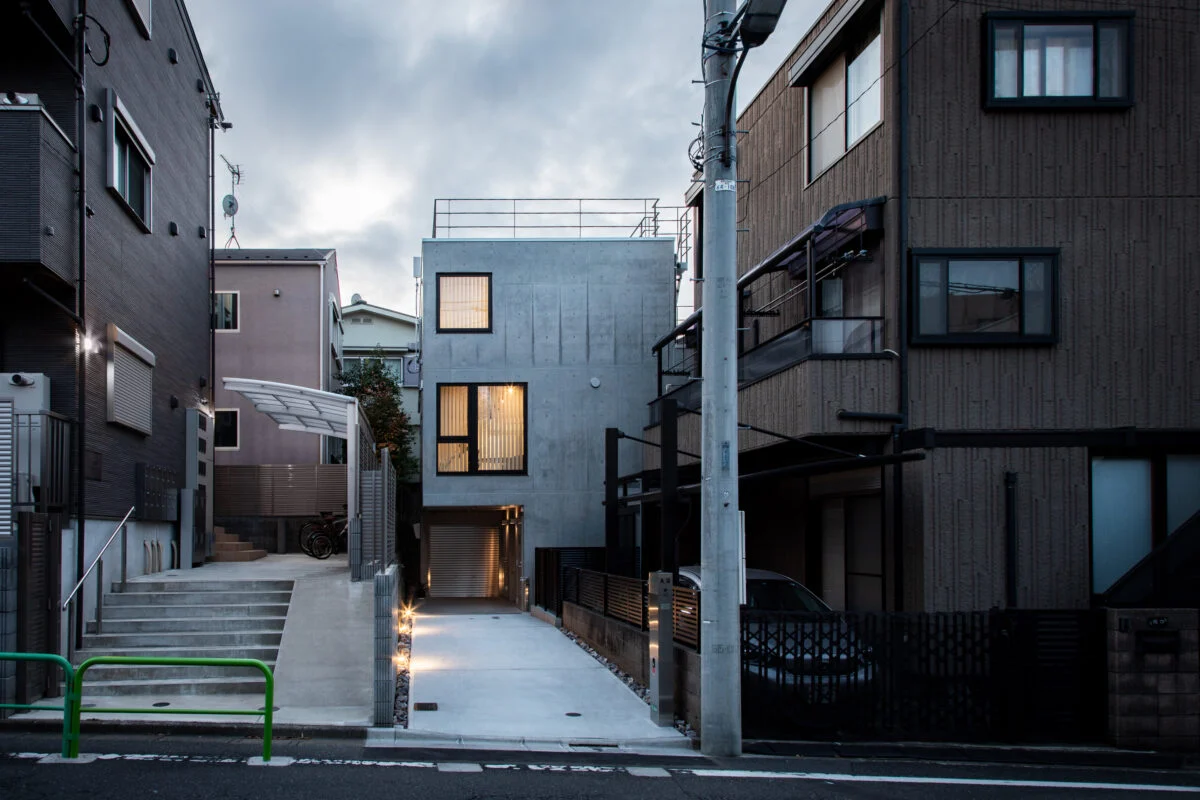 外観。画像中央奥が「武蔵関の住まい」。旗竿地のため道路まで距離があるという条件を生かし、道路に向かって大きく開口した。2階はLDKの窓。3階の窓は法的に必要な非常口でもある。大きさの違う正方形の窓をアクセントに、コンクリートの質感が引き立つデザインの外観とした