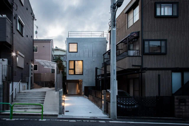外観。画像中央奥が「武蔵関の住まい」。旗竿地のため道路まで距離があるという条件を生かし、道路に向かって大きく開口した。2階はLDKの窓。3階の窓は法的に必要な非常口でもある。大きさの違う正方形の窓をアクセントに、コンクリートの質感が引き立つデザインの外観とした

