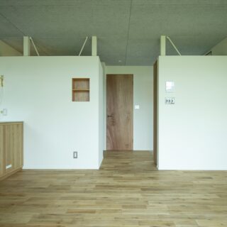 LDKから玄関や水回りの方向を見る。壁面の上部を空け天井を繋げたことに加え、中央の通路を出て右にある玄関とLDKの間に仕切りを設けず、より広い体感が得られる空間を実現した。壁の上部に見られる鉄骨はこの家が建った40年前からのもの