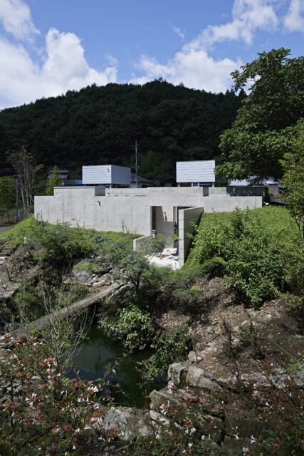 南東から家を見る。なだらかな丘に家が埋もれている。画像手前、既存の池はそのまま活用した