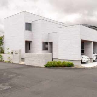 外観。横長に広い土地のため、建物をシンプルにすると圧迫感が出てしまう。そこで建物に変化をつけた。擁壁も高さだけでなく道路との距離を細かく変え、外壁と同じ仕上げにすることで圧迫感がないように工夫した。近隣の方からも好評で、地域のランドマークになっている