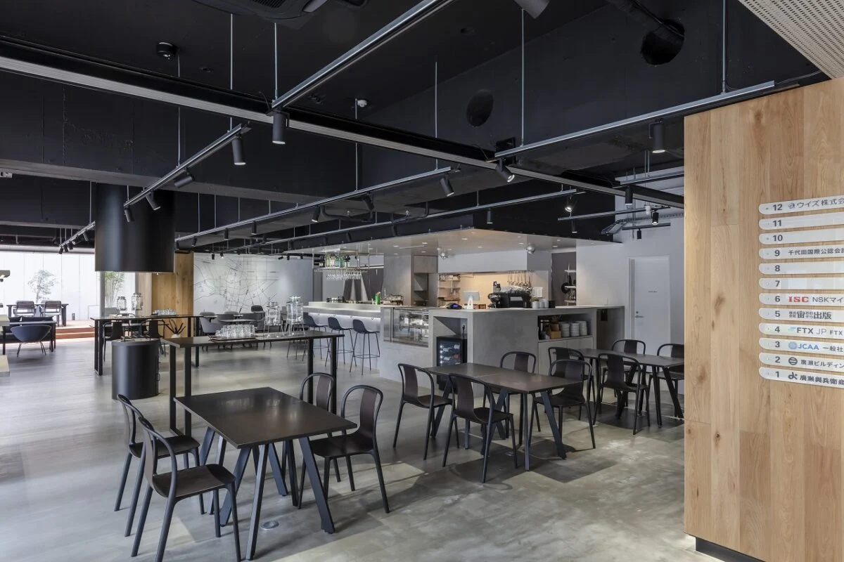 カフェダイニングのお客さまは南側（写真左）から入店。写真は、上階のオフィスへ向かう西側エントランスからの目線。天然木で仕上げた柱の奥（写真右）に進むとエレベーターがある。カフェダイニングとの仕切りがなく、オフィス利用者とのつながりも生まれやすい