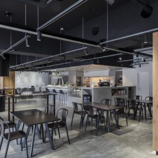 カフェダイニングのお客さまは南側（写真左）から入店。写真は、上階のオフィスへ向かう西側エントランスからの目線。天然木で仕上げた柱の奥（写真右）に進むとエレベーターがある。カフェダイニングとの仕切りがなく、オフィス利用者とのつながりも生まれやすい