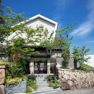 外観。家を建て替えるにあたり、鬱蒼としていた木々を整備するなど、まずは土地の整備から始めた。既存の石垣や画像中央の門扉などシンボル的なものは補強をしながら残したという。Sさまのさりげなくという意を汲み取り、家が木々で隠れるように計画
