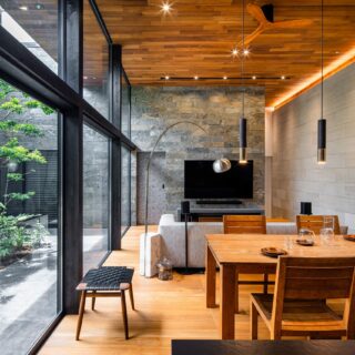 LDKの天井と床はチークの張り方を変え、上下が木でも重くならないように配慮。テレビの裏の壁は、黒雲母入りの石壁。一方、LDKで一番大きな壁はさらりとした表情の異なる砂岩水磨きを使用（写真右）。奥の石壁に負けない高級感を出しつつ、空間を重くしない素材を選んでいる