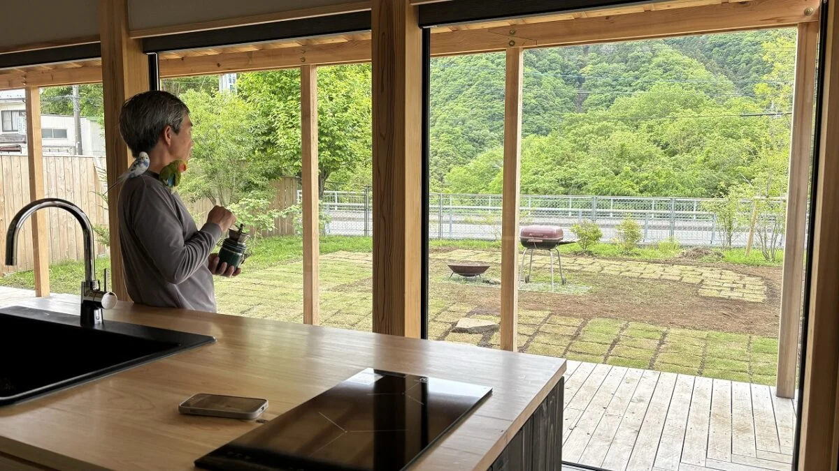 『MOKKEJA 青野原』でペットのインコを肩に乗せ、庭を眺める李さん。庭に思いきりひらいた室内からの眺めは抜群の開放感。緑豊かな里山の風景に心が和む