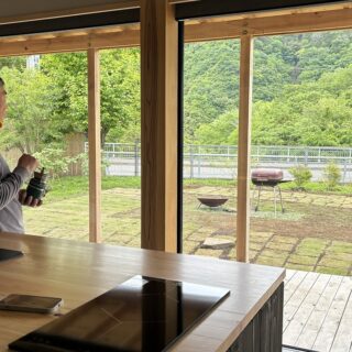 『MOKKEJA 青野原』でペットのインコを肩に乗せ、庭を眺める李さん。庭に思いきりひらいた室内からの眺めは抜群の開放感。緑豊かな里山の風景に心が和む