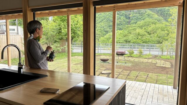 『MOKKEJA 青野原』でペットのインコを肩に乗せ、庭を眺める李さん。庭に思いきりひらいた室内からの眺めは抜群の開放感。緑豊かな里山の風景に心が和む