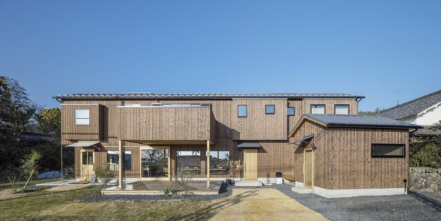 外観。道路に接する面がとても長い敷地の特徴を活かし、建物もあえて横長に。右手前の小屋は施主様の事務所。横長で大きく見える建物と、かわいらしい小屋の対比が印象的だ。特に意識したのが、2階のデザイン。建物が大きいので、外壁が平面だと圧迫感が出る。そのため、飛び出した部分を何か所か設けて変化をつけている
