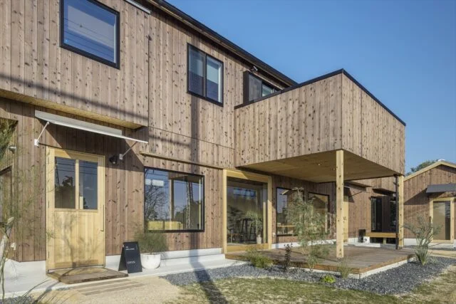 前庭から見た建物。1階がカフェで2階が住居スペースとなる。2階には広いベランダが設けられ、その下はカフェのテラス席として使用されている。1階のカフェには大きな窓を設置し、室内の明るさを確保している。また、人の手が触れる部分には木製の明るい部材を使用し、暖かみを感じられるように計算されている
