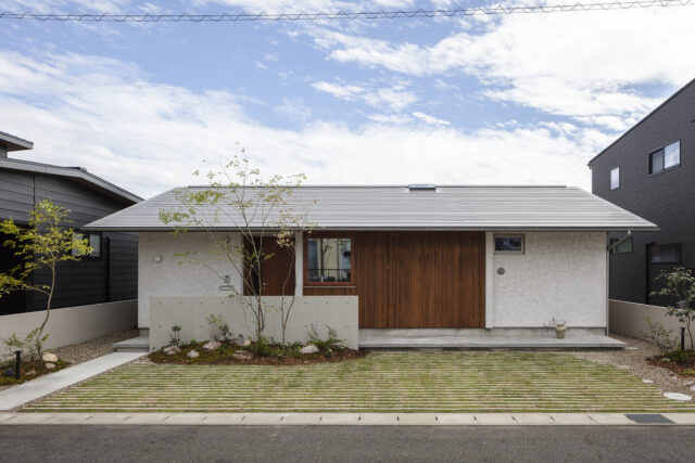 玄関側の外観。玄関前には建物の横幅と同じ長さで、ステップが設けられている。一段高くなったこのステップは、車止めを兼ねている。このため車止めがなく、スマートに見える。玄関前の植栽も、家の中からの見え方を考えて植えられている