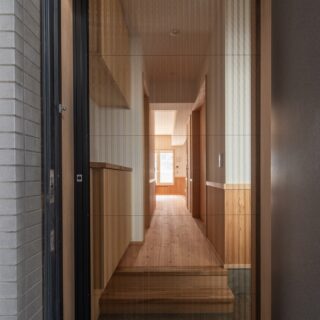 玄関の前から家を見る。玄関には網戸が入り、換気しやすい。まっすぐ視線が抜け、最奥の窓から外が見える