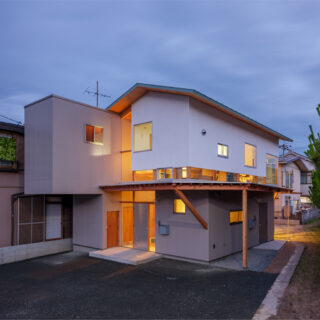 外観夕景。建物内から漏れ出る光が美しいだけでなく、1階にある親世帯のリビングから漏れる光が写真右側の里道を明るく照らす効果もある。照明がなく暗かった里道が明るくなったと、近隣の方にも好評だそうだ
