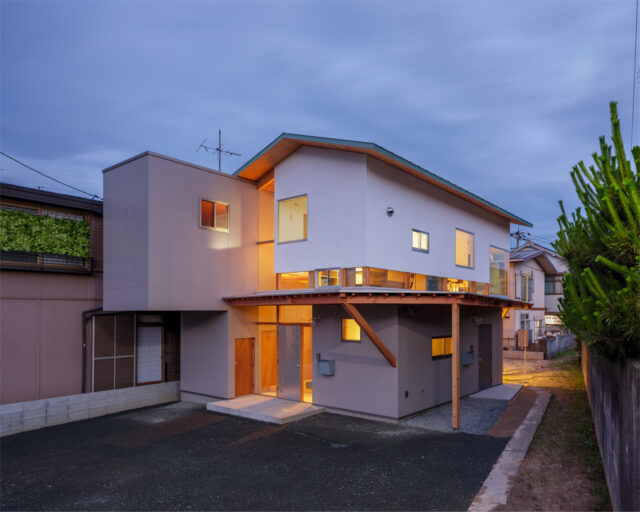 外観夕景。建物内から漏れ出る光が美しいだけでなく、1階にある親世帯のリビングから漏れる光が写真右側の里道を明るく照らす効果もある。照明がなく暗かった里道が明るくなったと、近隣の方にも好評だそうだ
