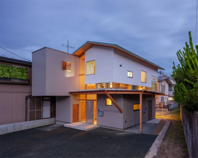外観夕景。建物内から漏れ出る光が美しいだけでなく、1階にある親世帯のリビングから漏れる光が写真右側の里道を明るく照らす効果もある。照明がなく暗かった里道が明るくなったと、近隣の方にも好評だそうだ
