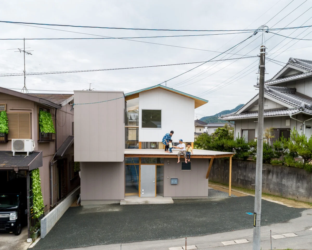 大きく張り出した庇は、きれいに手入れされた隣家の植栽とのつながりや平面的な広がりを考えて設置された。里道をはさんだ隣家の擁壁は2ｍの高さがあるため、まるで庇が隣家の地面につながっているように感じられる。同時に里道と敷地の、ゆるやかなつながりも実現している
